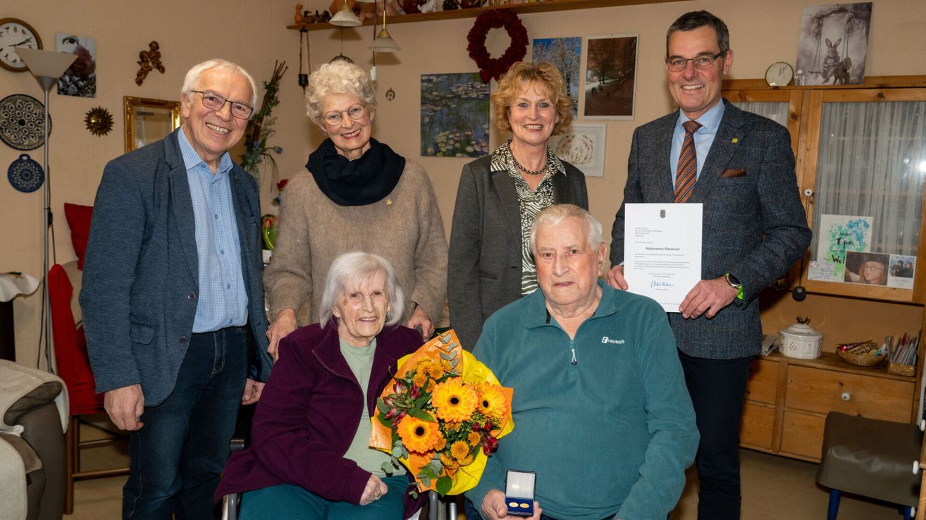 Eine Gruppe älterer Menschen posiert für ein Foto. Eine ältere Person hält einen Blumenstrauß. Eine Person hält ein Zertifikat.