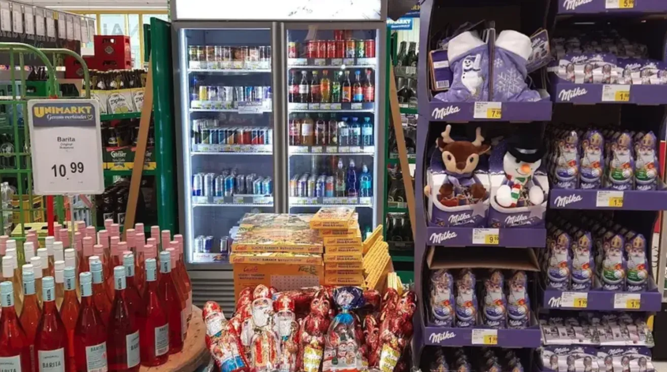 Ein Laden mit einem gekühlten Getränke- und Lebensmitteldisplay. Ein Regal mit Schokoladen und Spielzeug.