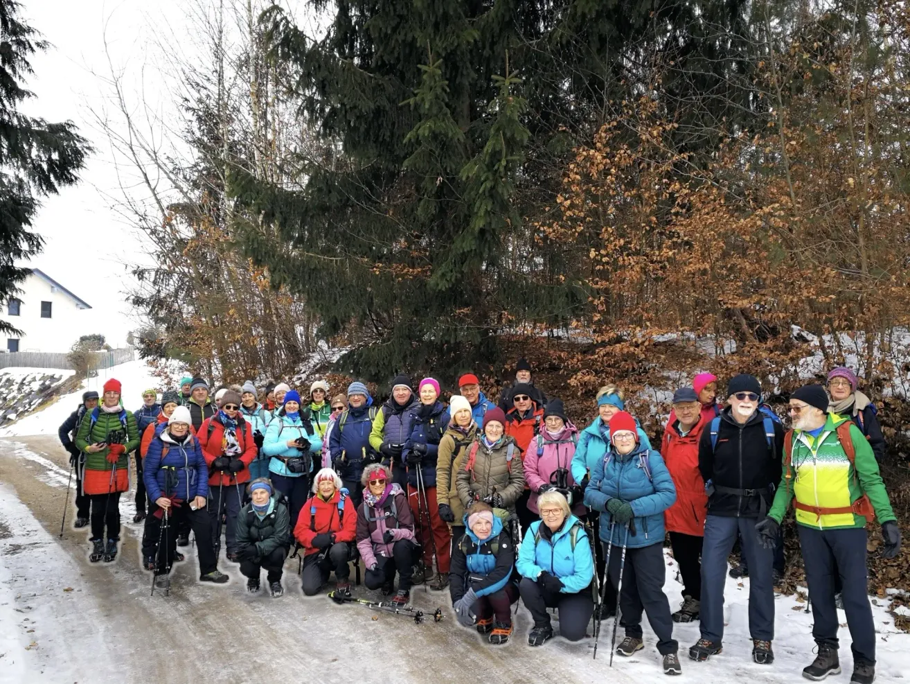 Eine Gruppe von Menschen posiert für ein Foto auf einem verschneiten Pfad, umgeben von Bäumen und in Winterkleidung gekleidet.