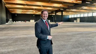 Ein Mann in einem Anzug steht mit lächelndem Gesicht in einem großen, leeren Lagerhaus.