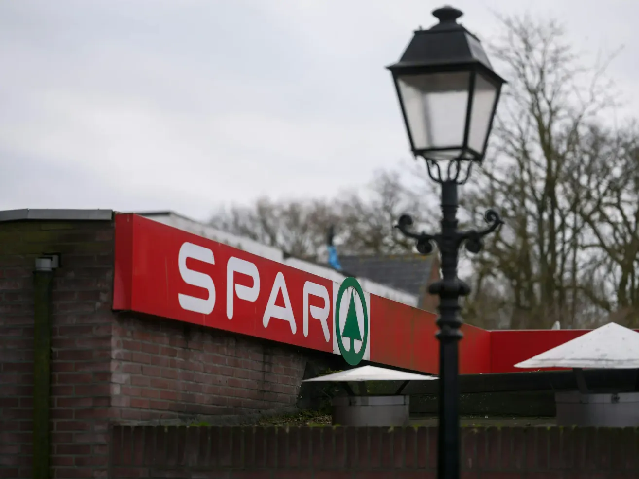 Ein rotes Backsteingebäude mit einem SPAR-Schild oben. Daneben steht eine schwarze Straßenlaterne mit Licht.