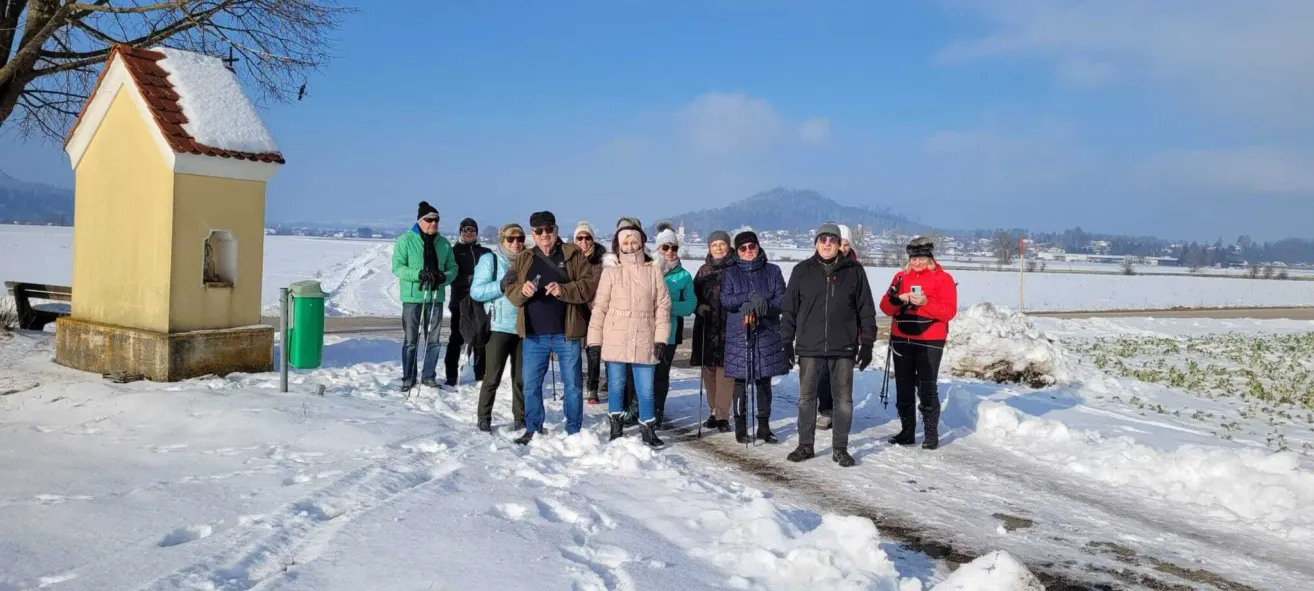 Eine Gruppe von Menschen, die warm gekleidet sind, steht in einem verschneiten Bereich mit Bergen im Hintergrund. Sie halten Skistöcke und einige tragen Brillen.