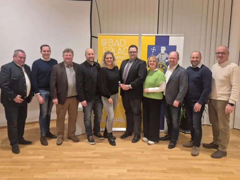 Eine Gruppe von Menschen steht auf einem Holzboden vor einem gelben und blauen Banner. Sie lächeln und scheinen für ein Foto zu posieren.