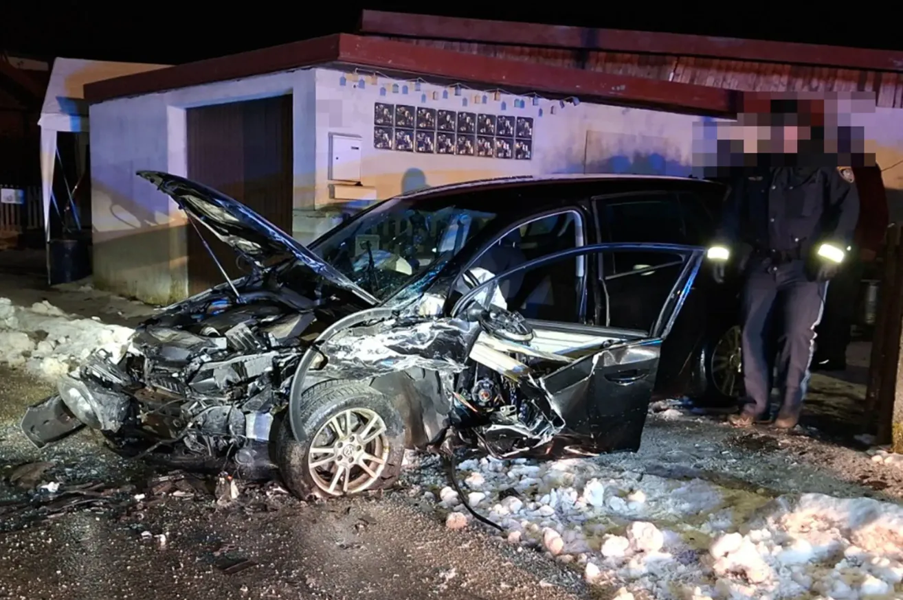 Ein schwarzes Auto vor einem Gebäude verunglückt, mit völlig demolierter Front und geöffneter Motorhaube.