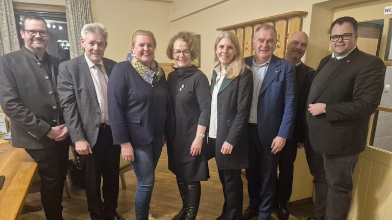 Eine Gruppe von fünf Erwachsenen, darunter Männer und Frauen, steht gemeinsam in einem Raum und lächelt für ein Foto.