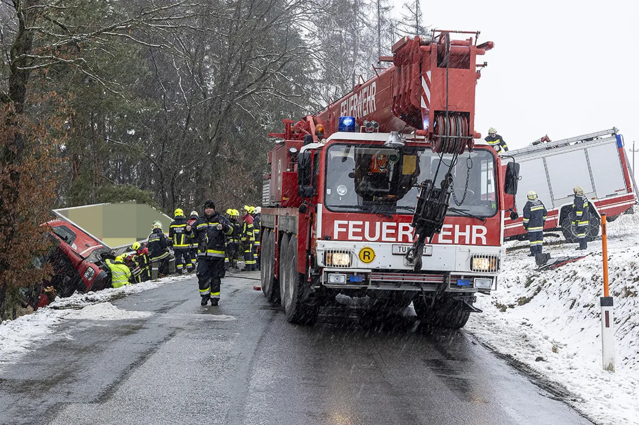 Ein roter Feuerwehrwagen steht an einem verschneiten Tag auf der Straße. Einige Feuerwehrleute sind am Straßenrand versammelt.