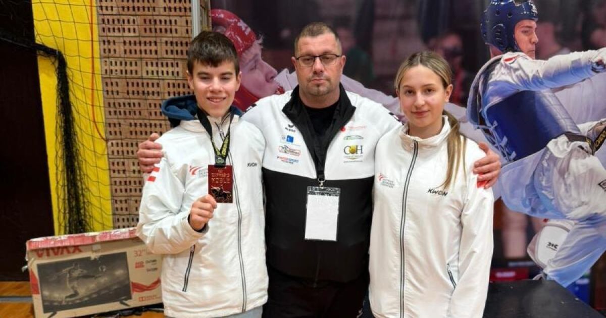 Drei Personen, zwei Jugendliche und ein Erwachsener, stehen nah beieinander, lächeln und haben einen unscharfen Hintergrund. Sie tragen weiße Jacken und Ausweise. Der erwachsene Mann hat eine Medaille.