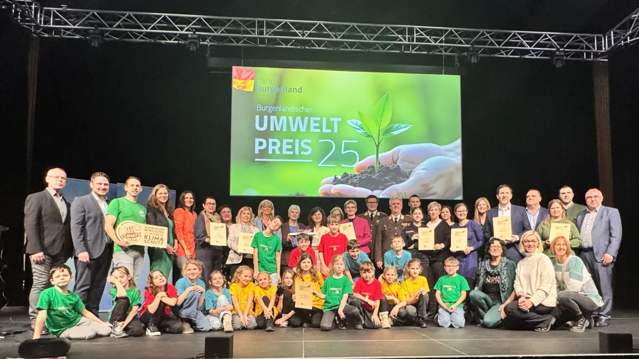 Eine Gruppe von Menschen auf der Bühne, die Auszeichnungen erhalten, ein großer Bildschirm im Hintergrund zeigt die Worte 'Burgenlandischer Umwelt Preis 25'.