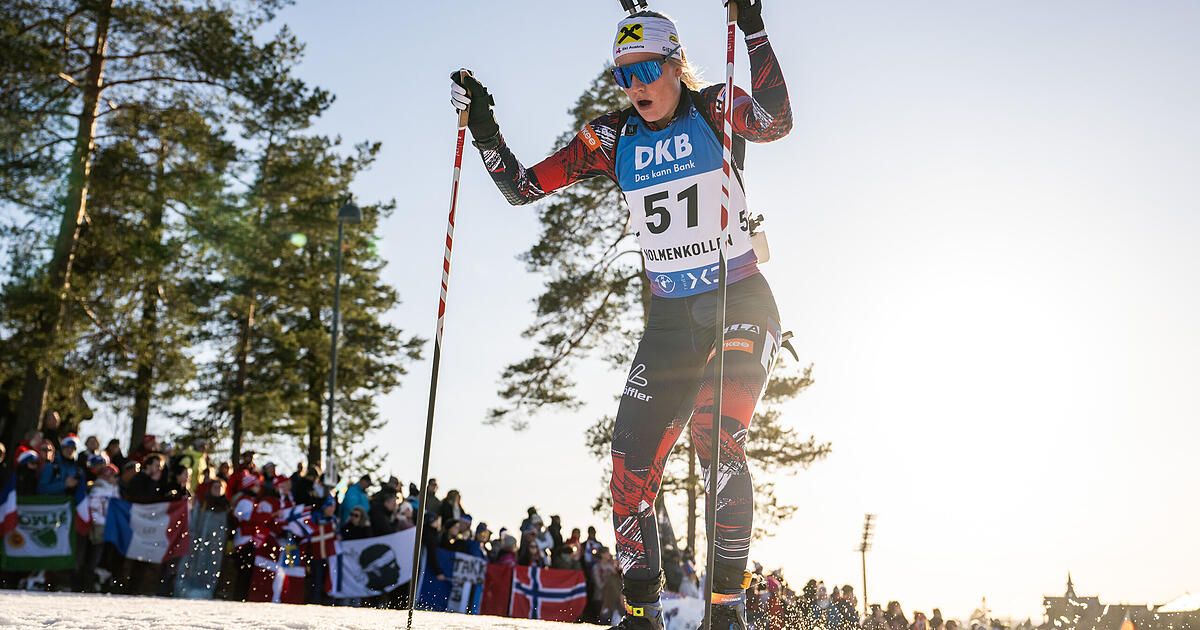 Eine Skifahrerin in einem roten und blauen Trikot mit 'DKB' und 'Das kann Bank' darauf. Sie hat die Nummer 51 auf der Brust. Sie fährt Langlauf und hält Skistöcke. Hinter ihr beobachtet ein Publikum das Event.