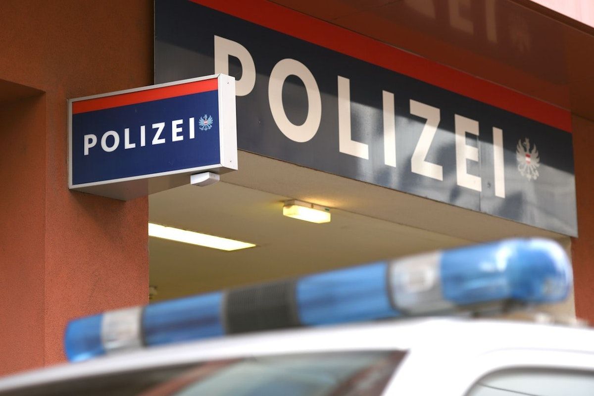 Eine Nahaufnahme eines blau-weißen Polizeischildes über einem Polizeiauto. Das Schild hat das Wort 'POLIZEI' in weiß auf blauem Hintergrund.