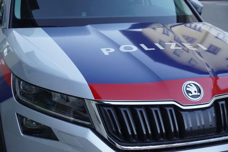 Nahaufnahme der Motorhaube eines Polizeiwagens mit blauen und roten Streifen und weissem 'POLIZEI'-Text. Die Frontgrille und Scheinwerfer des Autos sind sichtbar.
