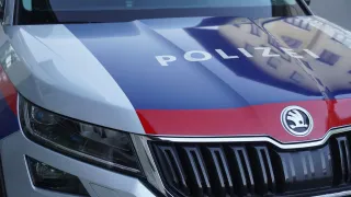 Nahaufnahme der Motorhaube eines Polizeiwagens mit blauen und roten Streifen und weissem 'POLIZEI'-Text. Die Frontgrille und Scheinwerfer des Autos sind sichtbar.