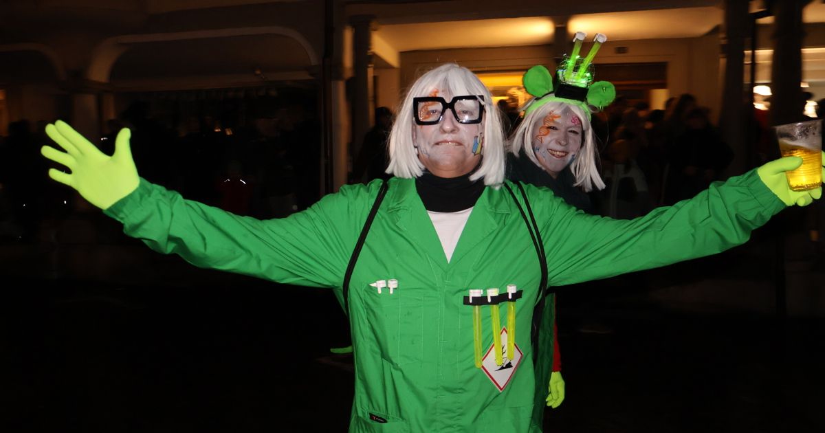 Zwei Personen in grünen Laborkittel posieren für ein Foto bei Nacht. Eine hat weiße Haare und weißes Gesichtsgemälde mit Brille, die andere grünes Gesichtsgemälde und einen grünen Hut mit Licht.