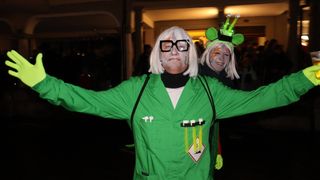 Zwei Personen in grünen Laborkittel posieren für ein Foto bei Nacht. Eine hat weiße Haare und weißes Gesichtsgemälde mit Brille, die andere grünes Gesichtsgemälde und einen grünen Hut mit Licht.