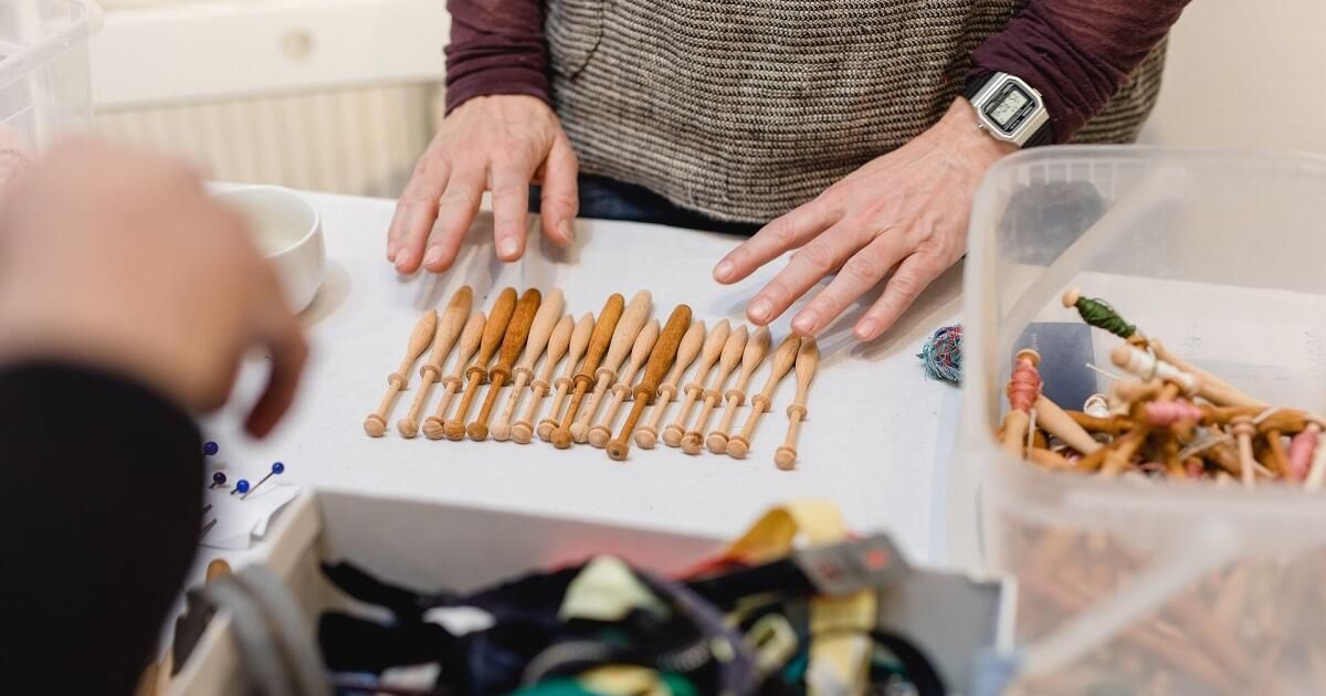 Eine Person ordnet kleine hölzerne Stricknadeln auf einem Tisch an, umgeben von Bastelmaterialien.