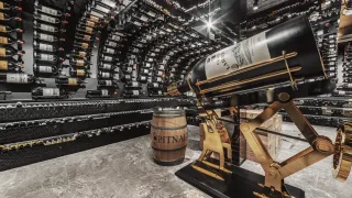 Ein Innenraumfoto eines großen Weinkellers, gefüllt mit zahlreichen Weinflaschen an den Regalen. Eine große Weinflasche mit dem Etikett Chateau Lafite ist prominent auf einem goldenen Ständer ausgestellt.