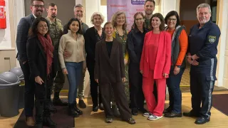 Eine Gruppe von Menschen steht für ein Foto zusammen, in verschiedenen Outfits, in einem Raum mit einem Banner dahinter.