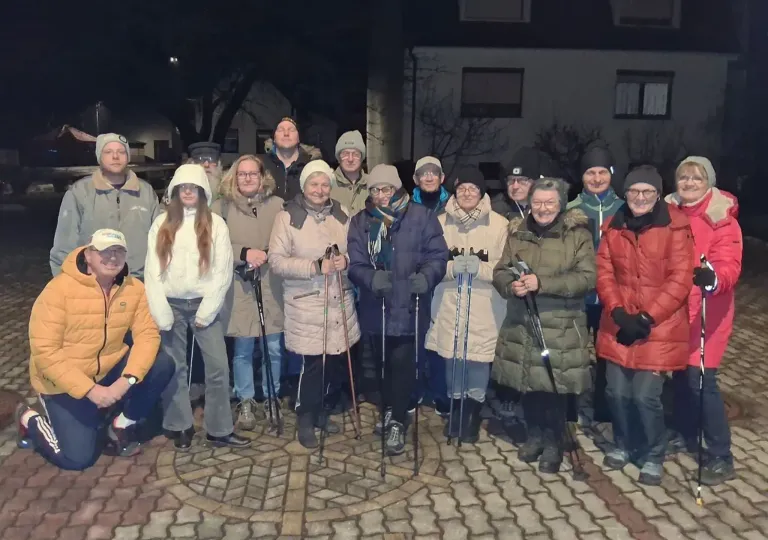 Eine Gruppe von Menschen, alle in Winterkleidung, steht nachts im Kreis draußen, hält Skistöcke und posiert für ein Foto.