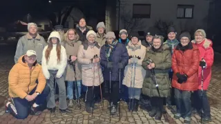Eine Gruppe von Menschen, alle in Winterkleidung, steht nachts im Kreis draußen, hält Skistöcke und posiert für ein Foto.