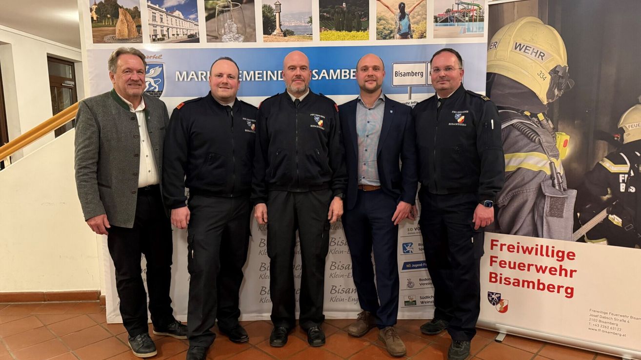 Fünf Männer in Uniform stehen zusammen vor einer Kulisse mit Bildern. Sie alle schauen zur Kamera.