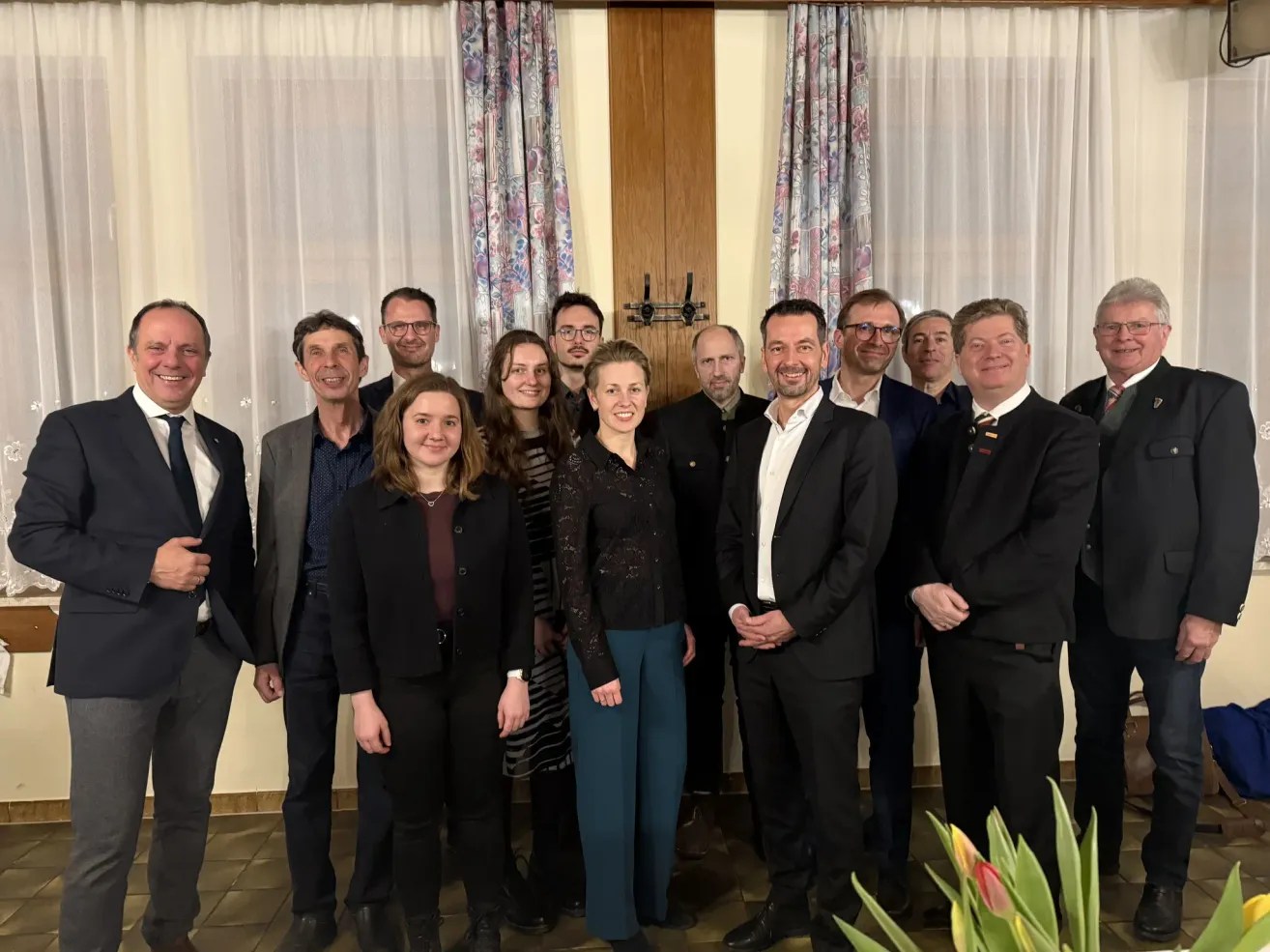 Eine Gruppe von Personen in formeller Kleidung posiert für ein Foto vor einer Holztür mit Blumenvorhängen.