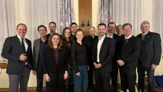 Eine Gruppe von Personen in formeller Kleidung posiert für ein Foto vor einer Holztür mit Blumenvorhängen.