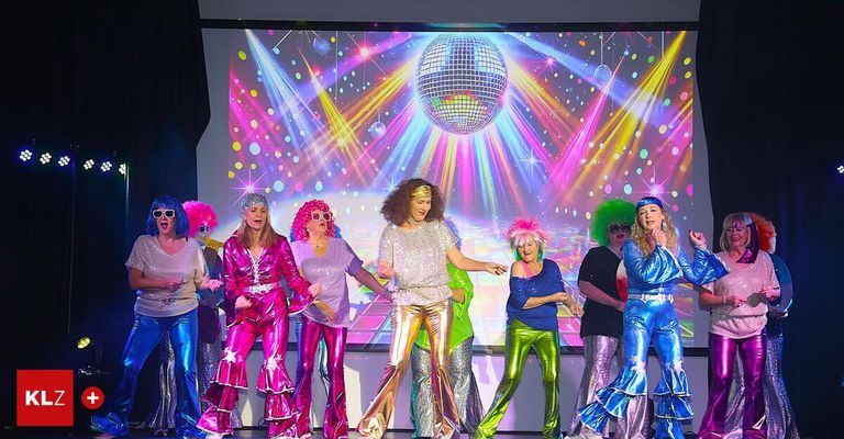 Eine Gruppe von Frauen in Disco-Kostümen der 70er Jahre tritt auf der Bühne auf, mit einer leuchtenden Discokugel im Hintergrund.