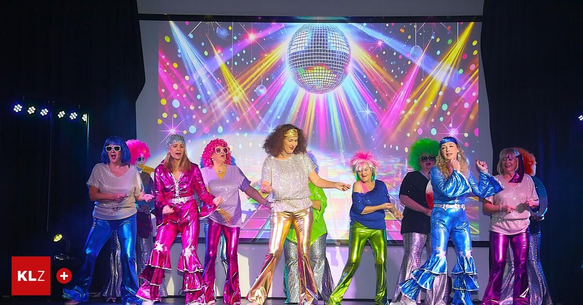 Eine Gruppe von Frauen in Disco-Kostümen der 70er Jahre tritt auf der Bühne auf, mit einer leuchtenden Discokugel im Hintergrund.