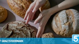 Die Hände einer Person berühren verschiedene Arten von Brot auf einer weißen Oberfläche, möglicherweise in Vorbereitung auf das Backen oder Essen. Die Brote haben unterschiedliche Formen und Texturen.