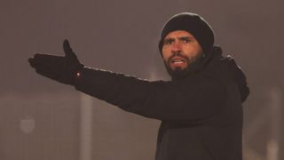 Ein Mann in einer schwarzen Mütze und einem schwarzen Mantel zeigt mit seiner rechten Hand und trägt einen Handschuh mit rotem Licht.