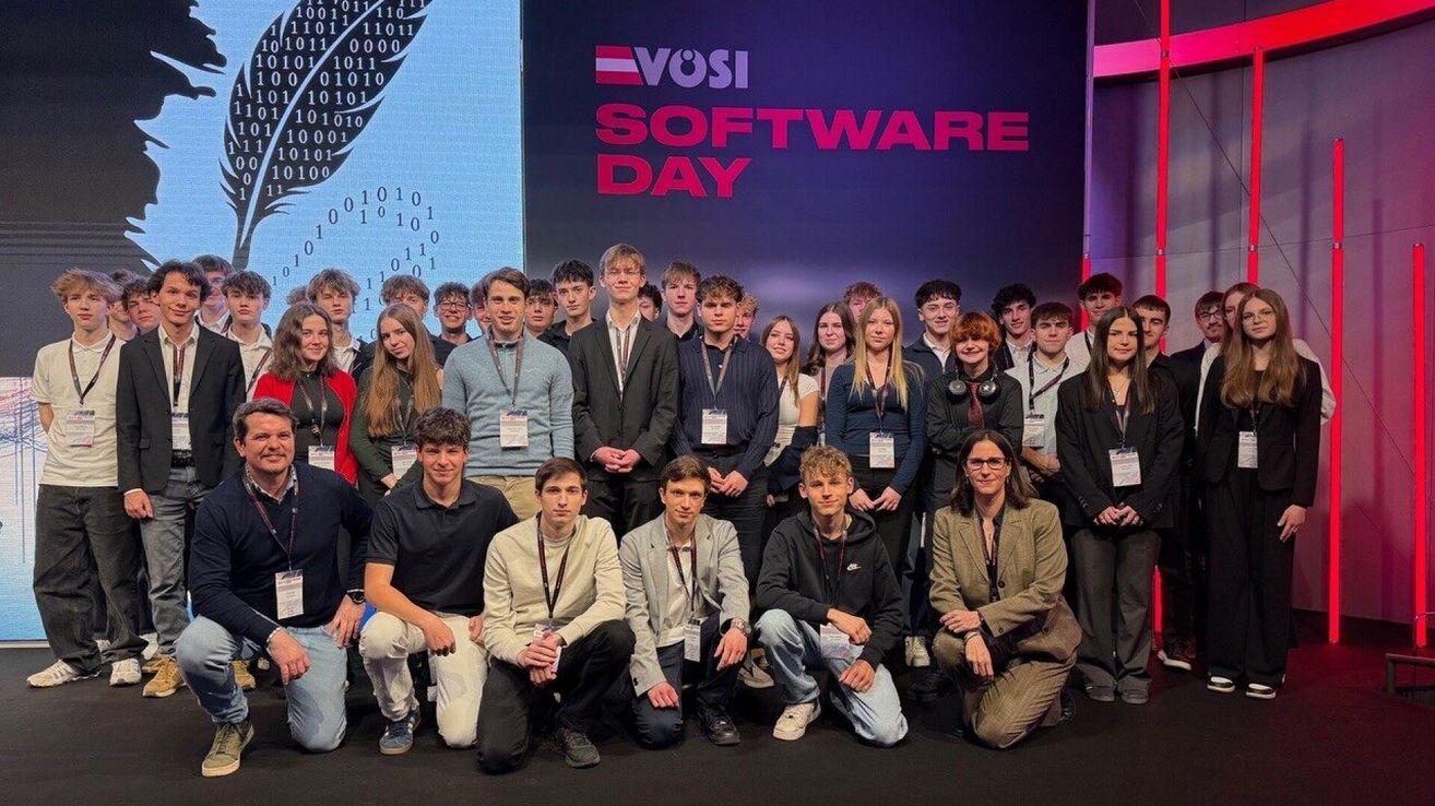 Eine Gruppe junger Erwachsener posiert für ein Foto bei einer Veranstaltung, mit einem digitalen Hintergrund, der die Worte 'VOSI SOFTWARE DAY' anzeigt. Sie tragen alle Namensschilder und einige lächeln.