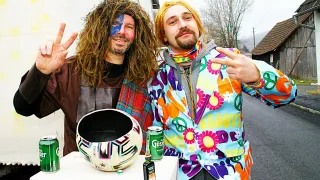 Zwei Männer posieren für ein Foto. Einer trägt ein braunes Shirt und hat blaue Gesichtsbemalung. Der andere ist in einem farbenfrohen Blumenmantel. Auf dem Tisch stehen ein Fußball, eine Flasche und zwei grüne Dosen.