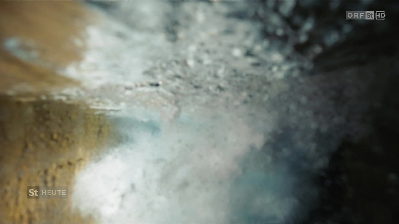 Eine Nahaufnahme einer nassen Oberfläche, möglicherweise durch Regen, mit einer Mischung aus Grau- und Blautönen und kleinen Wassertropfen.