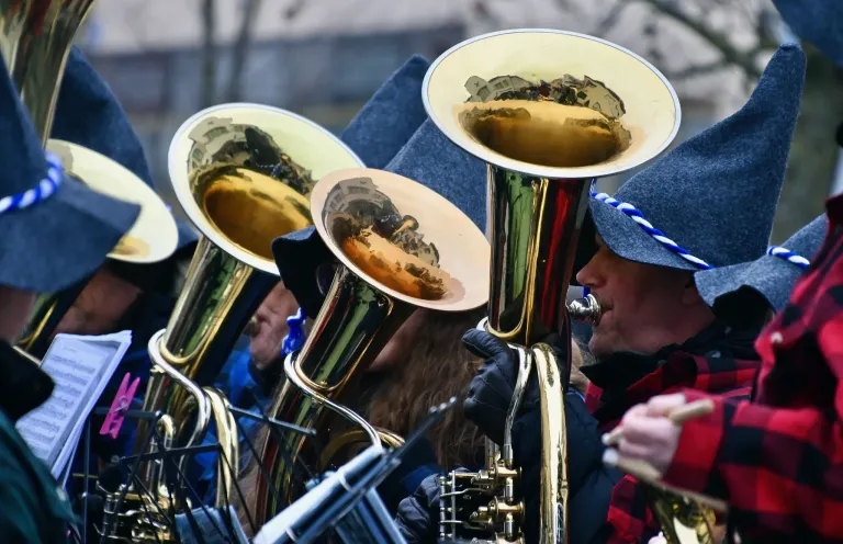 Eine Gruppe von Musikern spielt Blechblasinstrumente bei einer Veranstaltung im Freien. Sie tragen Mützen und Handschuhe. Die Instrumente stehen eng beieinander, und einige Reflexionen sind auf den Instrumenten sichtbar.