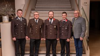Fünf Männer in Militäruniformen stehen auf einer Treppe und lächeln für ein Foto. Sie tragen braune Uniformen mit roten Besätzen und Abzeichen auf der Brust.
