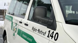 Nahaufnahme eines weißen und grünen Fahrzeugs mit den Worten 'Alpin-Notruf 140' und einem Logo auf der Tür.