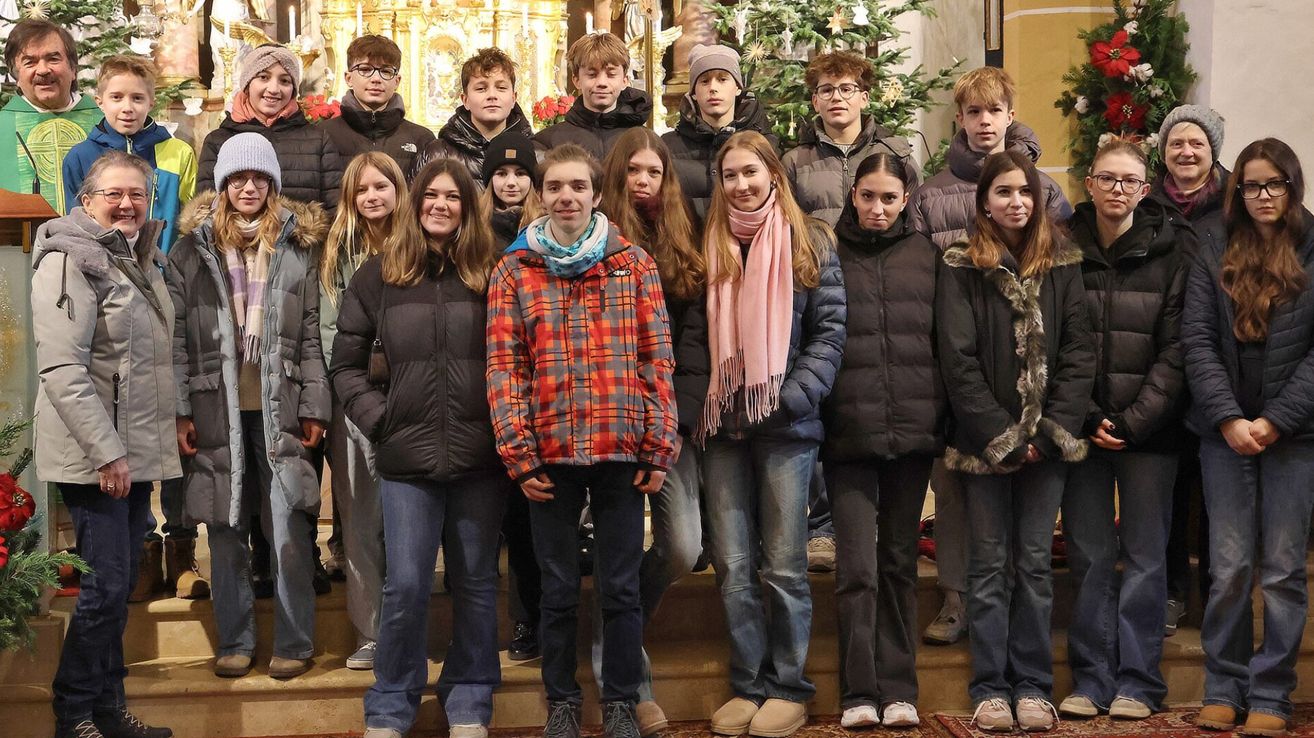 Eine Gruppe junger Menschen, sowohl Jungen als auch Mädchen, posiert für ein Foto vor einem geschmückten Weihnachtsbaum und Altar.