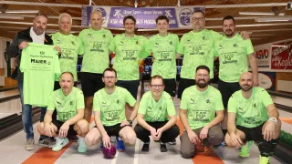 Eine Gruppe von Männern in grünen Trikots mit Logos posiert für ein Foto. Einige stehen, andere hockten, und sie alle sehen glücklich aus. Hinter ihnen ist ein Banner mit einem Logo und etwas Text.