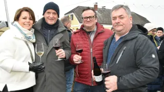 Vier Erwachsene lächeln, halten Weingläser in der Hand und posieren für ein Foto im Freien. Dahinter steht ein Haus und eine Straßenlaterne.