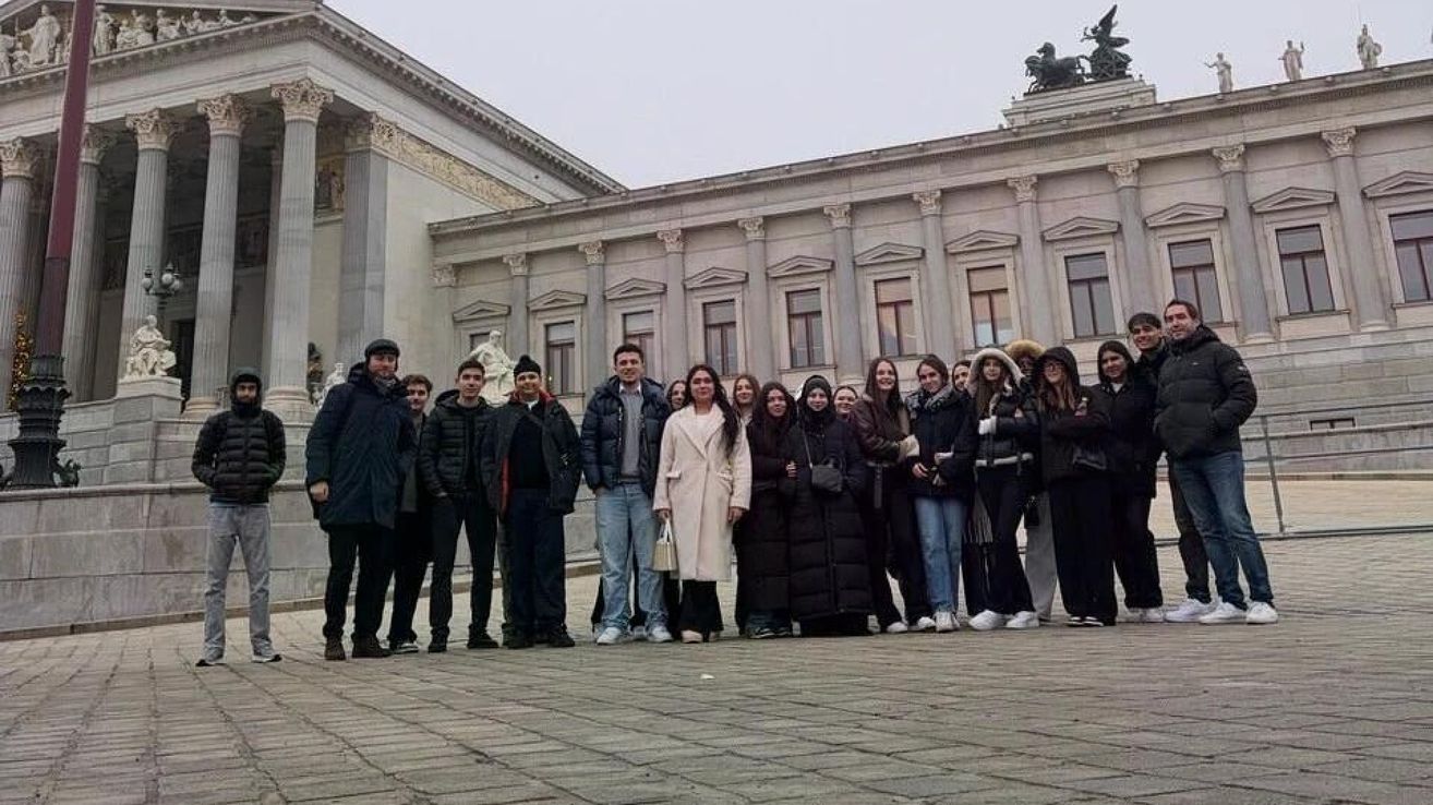 Eine Gruppe von Menschen in Winterkleidung posiert für ein Foto vor einem großen Gebäude mit klassischer Architektur und einer Statue auf der Spitze.