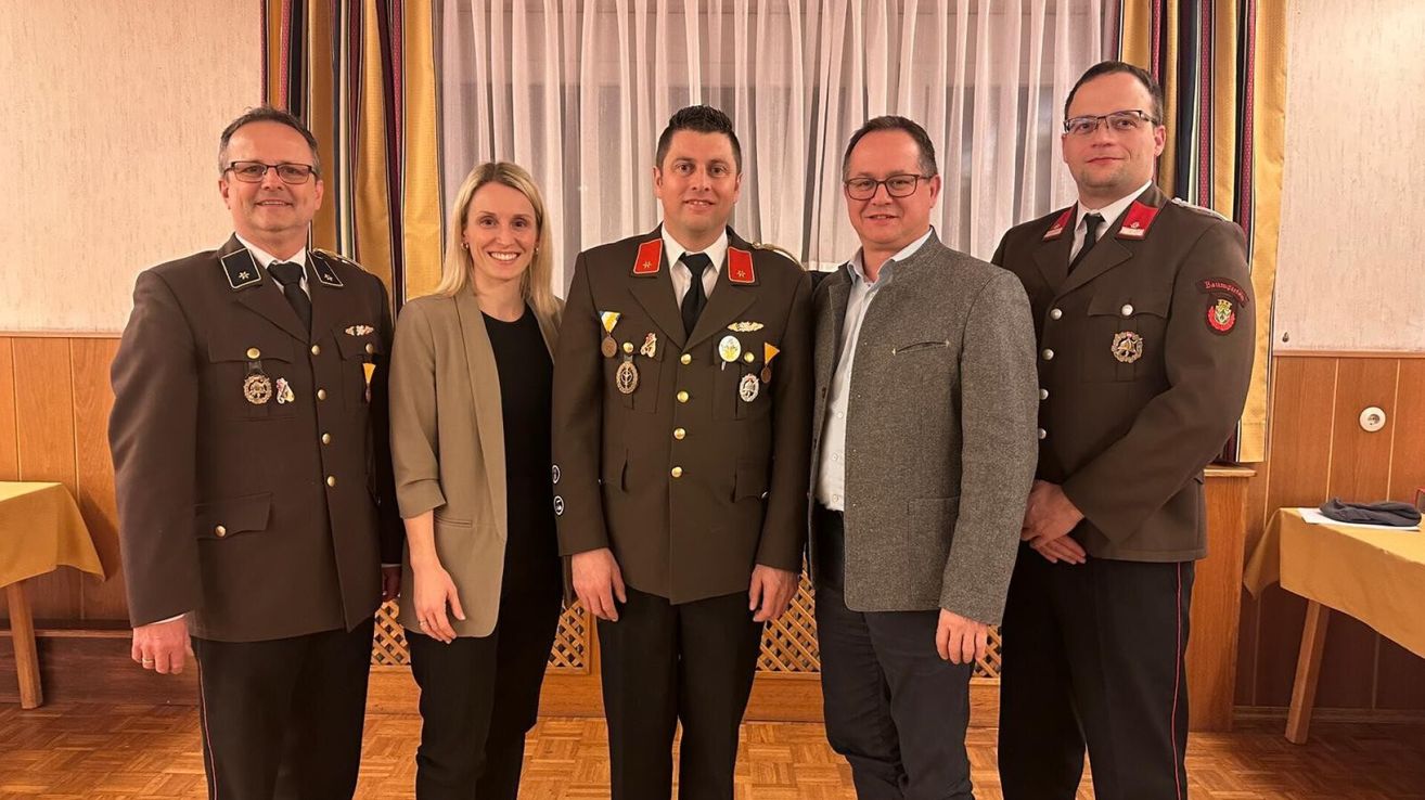 Fünf Personen stehen zusammen in einem Innenraum; eine Frau und vier Männer. Drei der Männer tragen Militäruniformen.