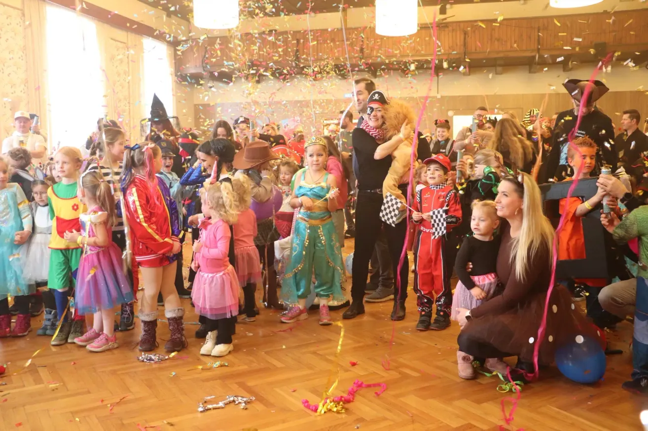 Eine Gruppe von Kindern und Erwachsenen in einem Saal, alle in Kostümen, feiern mit fallendem Konfetti. Ein Mann in Piratenkostüm hält ein Kuscheltier.