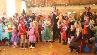 Eine Gruppe von Kindern und Erwachsenen in einem Saal, alle in Kostümen, feiern mit fallendem Konfetti. Ein Mann in Piratenkostüm hält ein Kuscheltier.