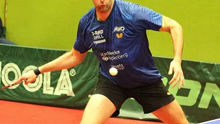 Ein Mann in einem blauen Shirt mit dem Wort "Newo" darauf spielt Tischtennis. Er trägt einen Stirnband und hat einen Tischtennisball in der Hand.