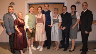 Eine Gruppe von Menschen in traditioneller Kleidung posiert für ein Foto in einem Raum. Zwei Frauen und zwei Männer stehen hinten.