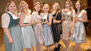 Eine Gruppe von Frauen in traditioneller Kleidung, möglicherweise für ein Fest, posiert für ein Foto mit Weingläsern in der Hand. Sie lächeln für die Kamera und vermitteln eine festliche Atmosphäre.