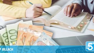 Eine Person mit einem Stift schreibt auf ein Buch mit Bargeld auf dem Tisch.