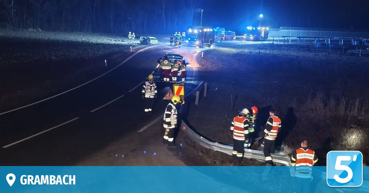 Rettungsdienste sind an einer nächtlichen Unfallstelle mit zwei Fahrzeugen, eines auf der Straße und eines in einem Graben. Helfer in reflektierenden Westen und Helmen kümmern sich um die Fahrzeuge und Personen.