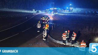 Rettungsdienste sind an einer nächtlichen Unfallstelle mit zwei Fahrzeugen, eines auf der Straße und eines in einem Graben. Helfer in reflektierenden Westen und Helmen kümmern sich um die Fahrzeuge und Personen.