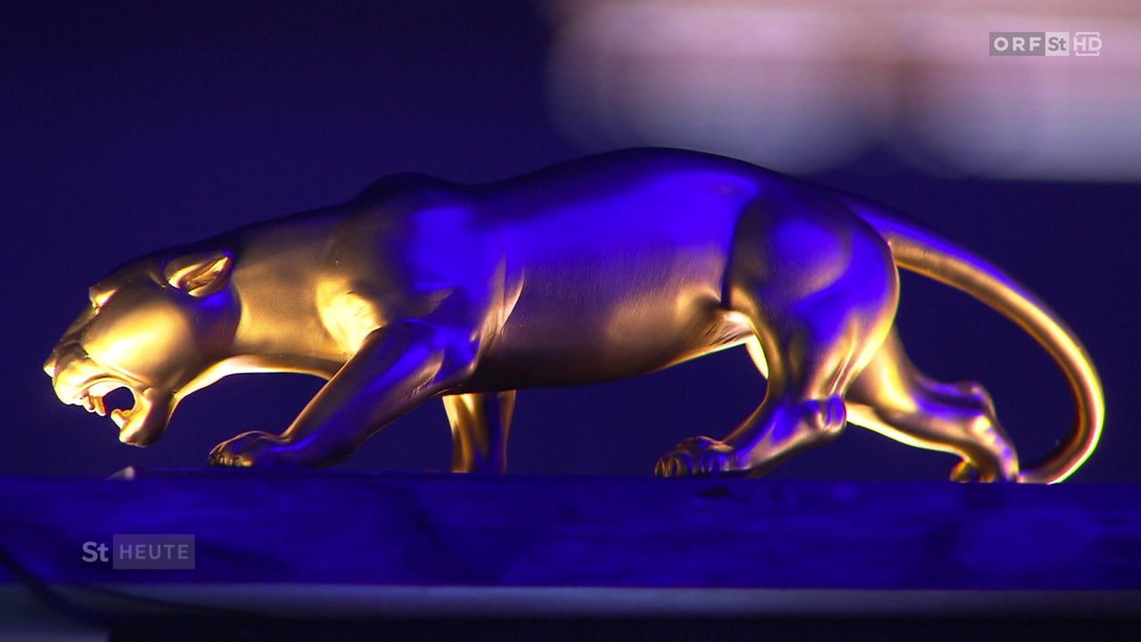 Eine goldene Skulptur eines Leoparden, beleuchtet mit einem violetten Licht, scheint sich in einer dunklen Umgebung zu bewegen.